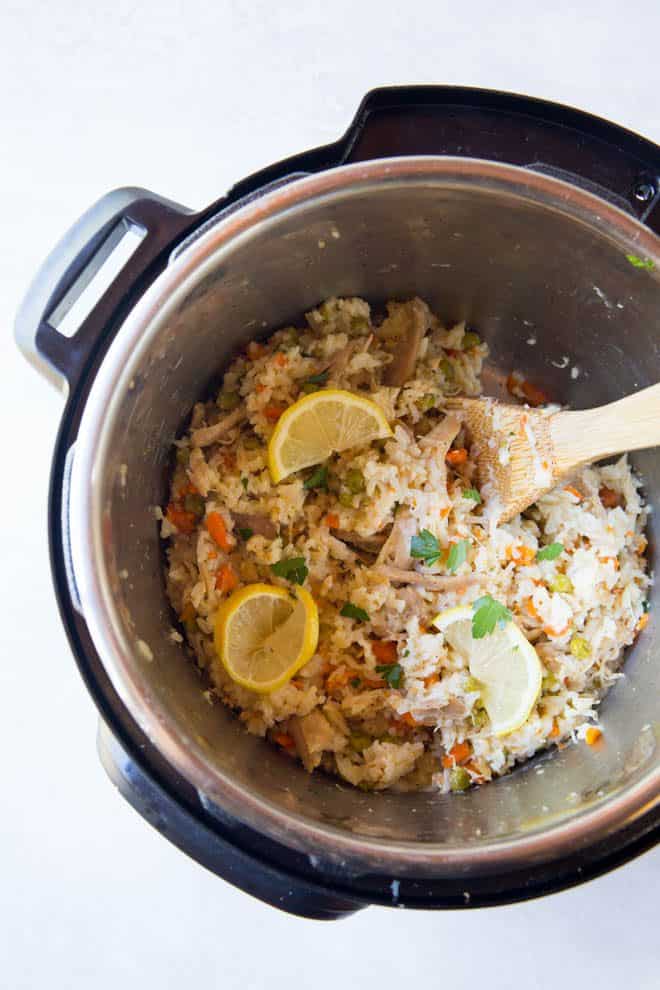 Cooked chicken and rice is sitting in the instant pot. A wooden spoon is scooping the rice.