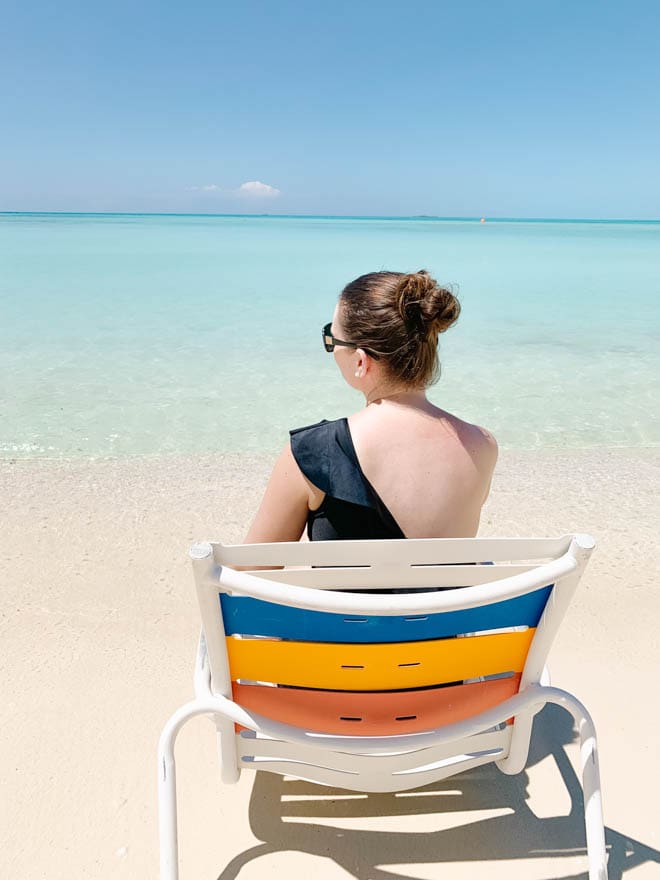 woman sitting in a chair on the beach in the bahamas with calm clear water.