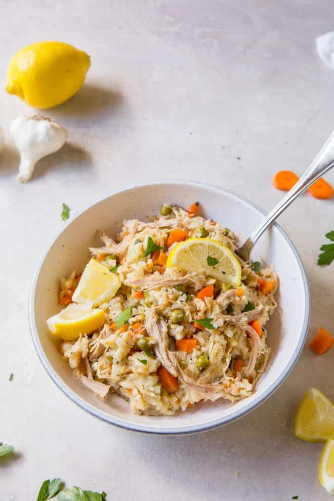 Chicken and rice is sitting in a while bowl on a white table. The bowl has a fork in it.