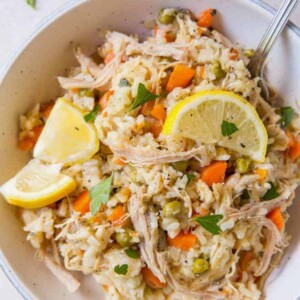 A large bowl of chicken and rice with two slices of lemon on top sitting on a white table.