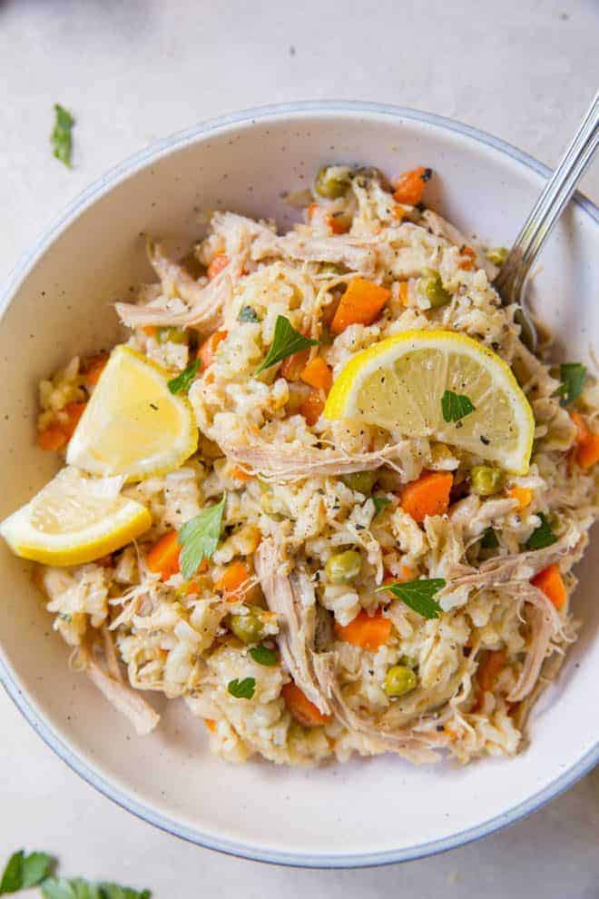 A large bowl of chicken and rice with two slices of lemon on top sitting on a white table.