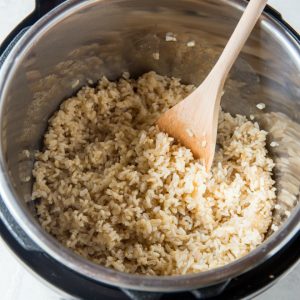 An open instant pot with cooked brown rice and a wooden spoon.