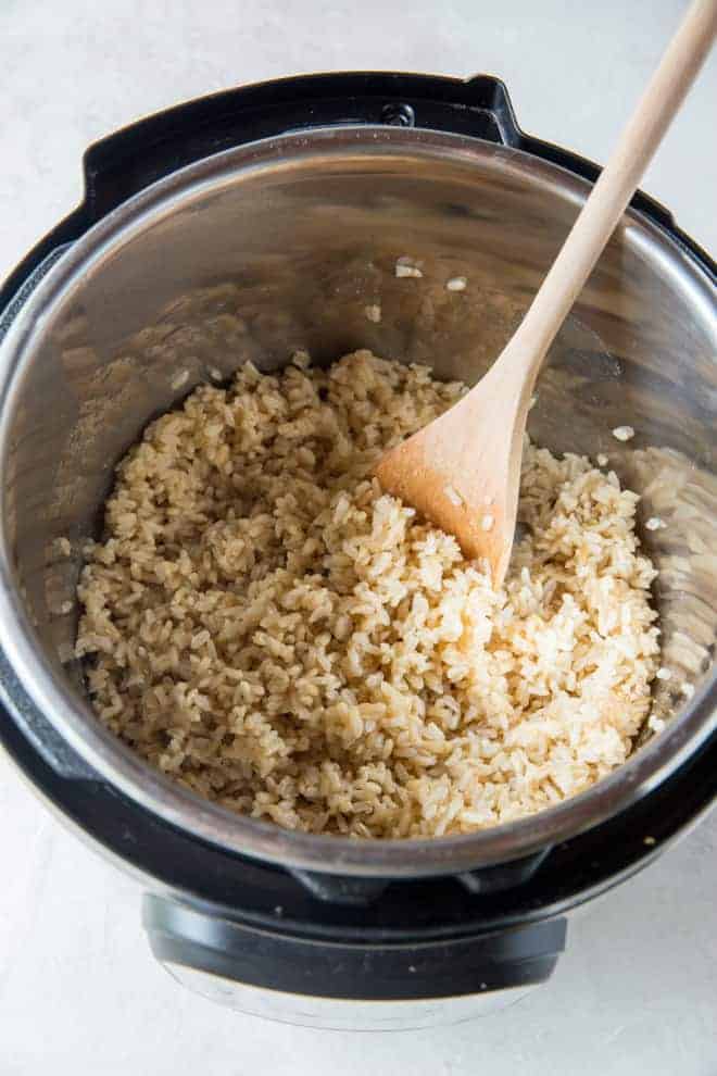 An open instant pot with cooked brown rice and a wooden spoon.