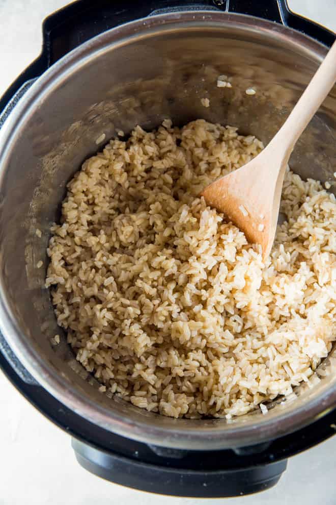 An open instant pot filled with cooked brown rice and a wooden spoon.