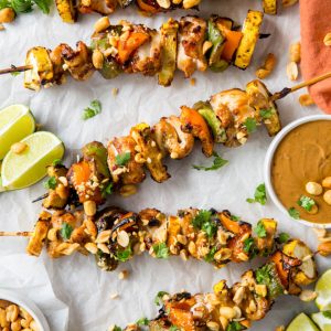 Five chicken kebabs sitting on a white background with peanut sauce on the side in a bowl.