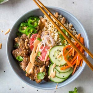 A bowl filled with brown rice, pork tenderloin, pickled veggies and sriracha mayo.