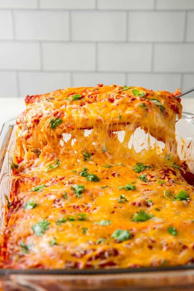 A spatula removes a turkey enchilada from the casserole dish.