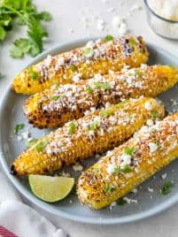 Four pieces of Mexican street corn sitting on a blue plate.