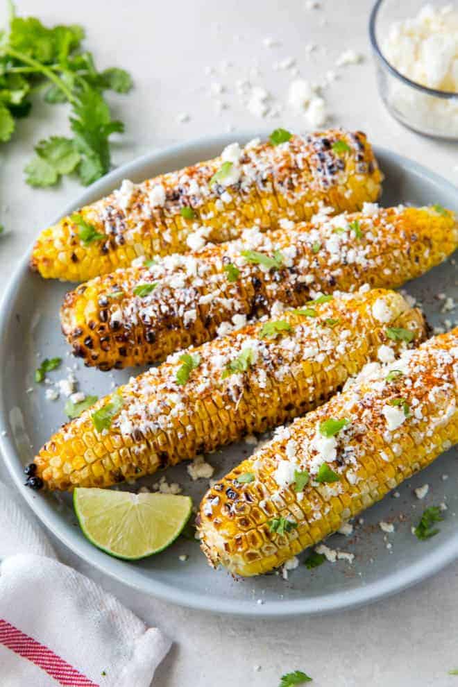 Four pieces of Mexican street corn sitting on a blue plate.