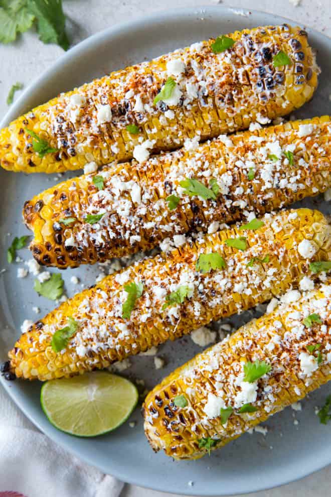 Four pieces of Mexican elote corn on the cob sitting on a plate.