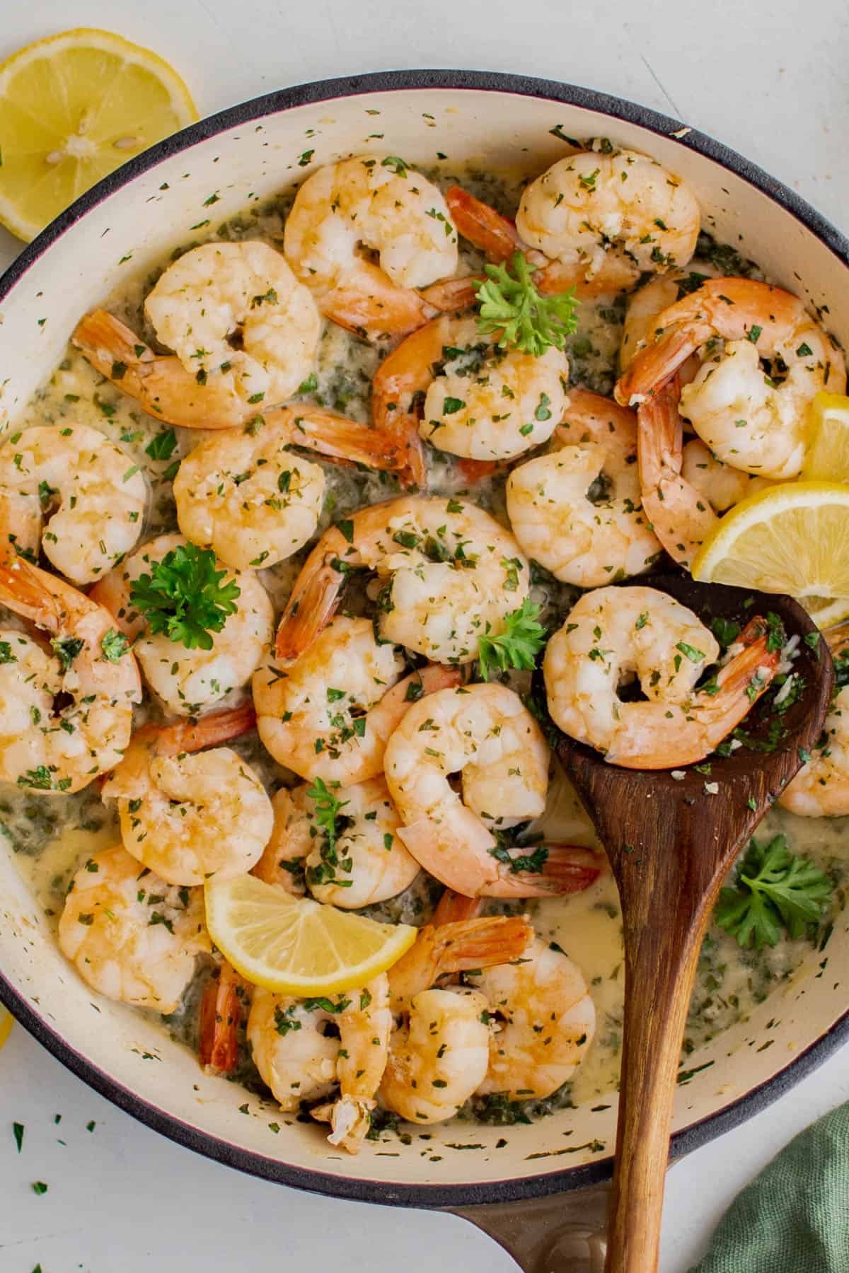 A skillet with cooked lemon garlic shrimp and a wooden spoon lifting the shrimp out of the pan.