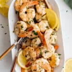 Cooked lemon garlic shrimp on a white serving plate with serving fork and lemon wedges.