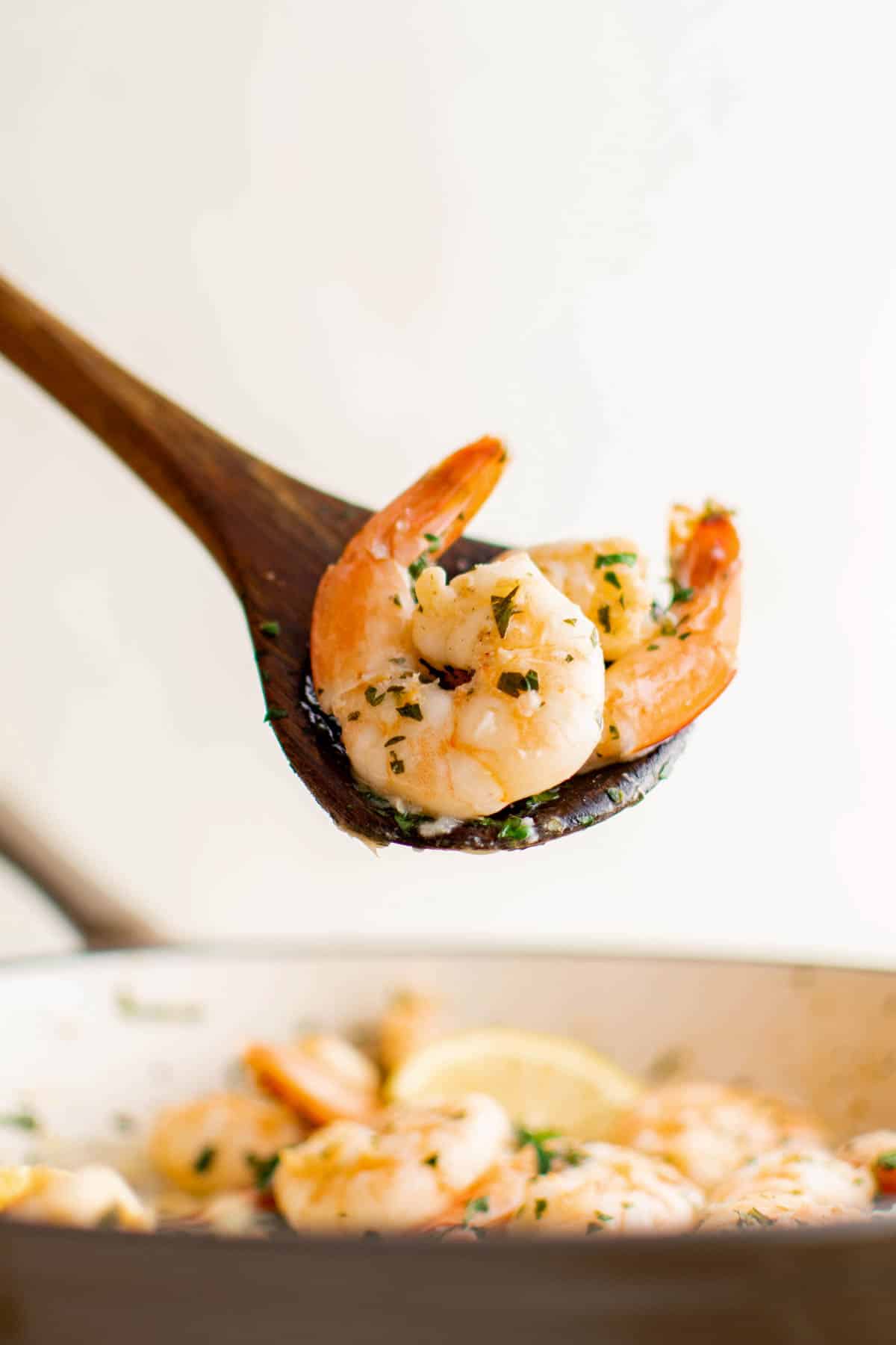 A wooden spoon serving two pieces of lemon garlic shrimp from the pan.