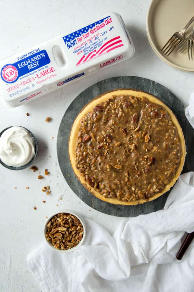A pecan pie cheesecake sitting on a white counter with a crate of Eggland's Best eggs off to the side.