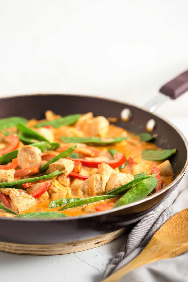 Coconut chicken curry in a skillet with red peppers, snow peas, and creamy coconut curry sauce