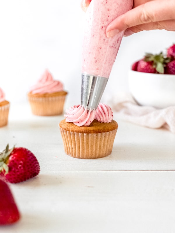 Pipping strawberry frosting onto cupcakes.