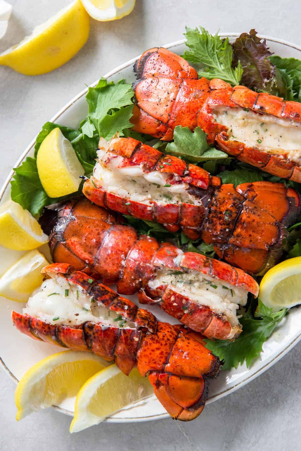 Four grilled lobster tails on a bed of lettuce on a plate for serving.