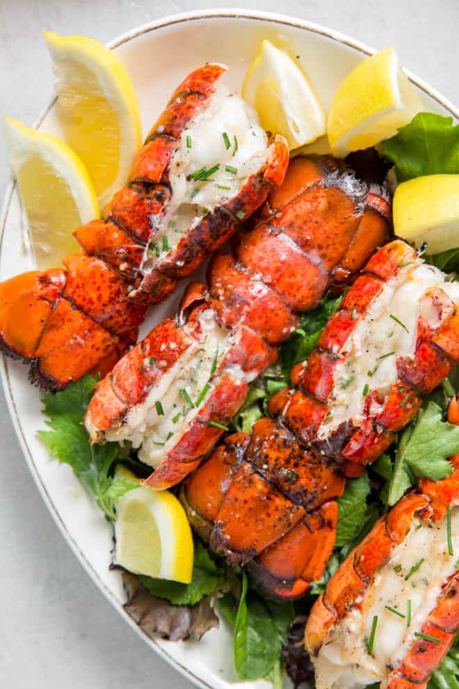 Close up of four grilled lobster tails on a plate with lemon wedges.