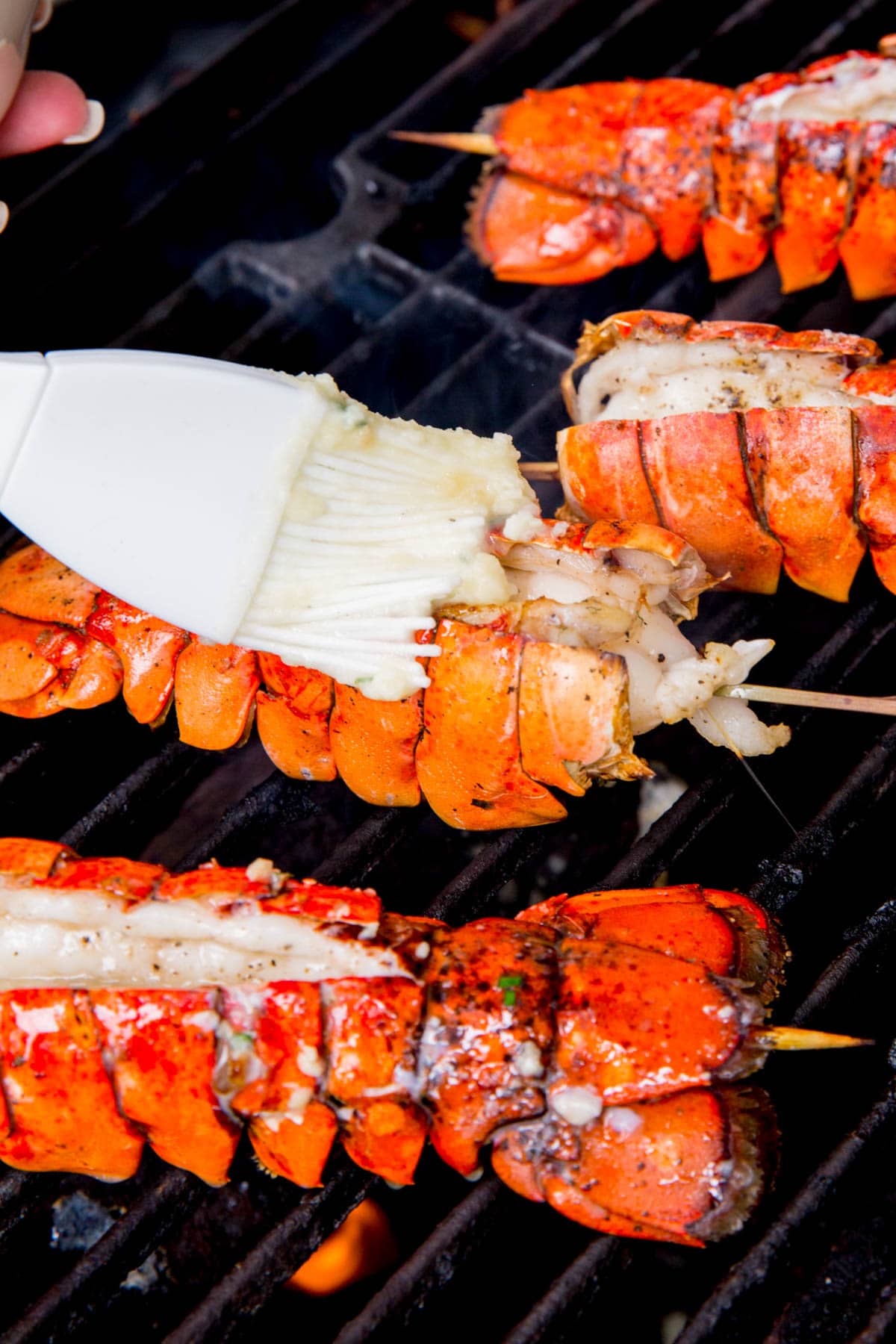 Spreading garlic butter sauce on lobster tails on the grill.