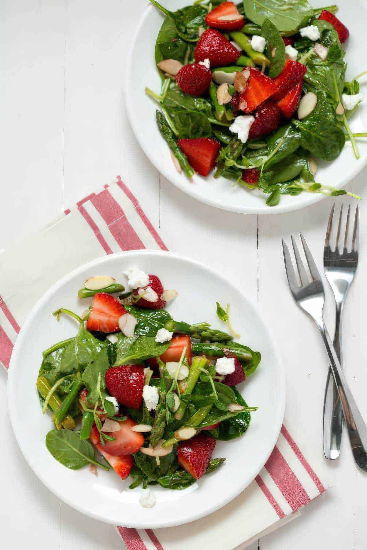 Two plates of strawberry spinach and asparagus salad with fresh strawberries, asparagus, and spinach.