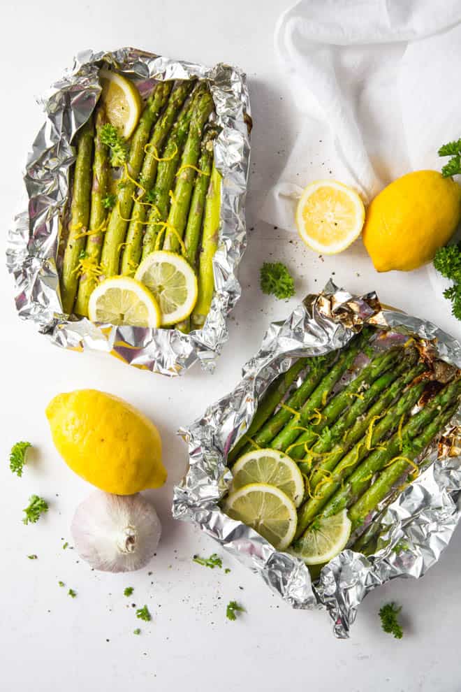 Two packets of grilled asparagus with lemon slices and lemon zest.