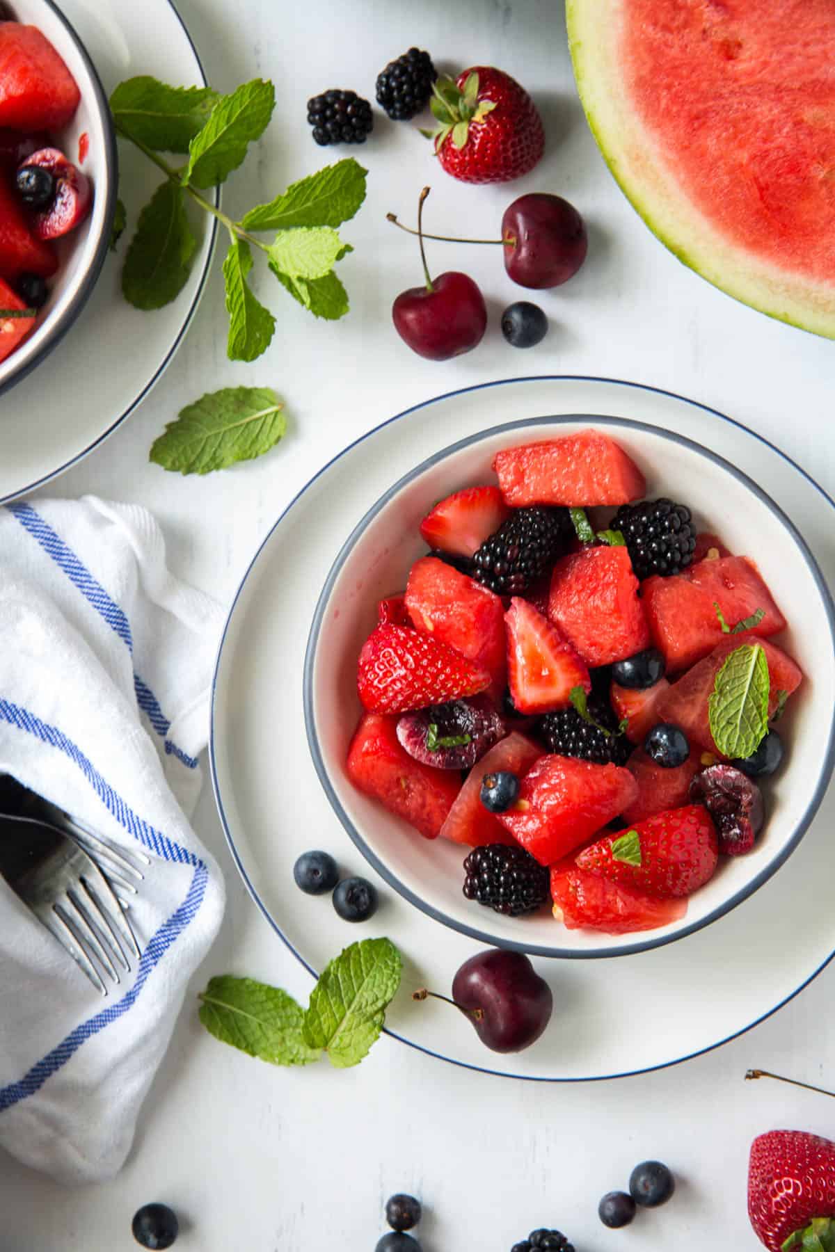 One white bowl filled with watermelon fruit salad sitting on a white table. Fresh mint is garnished on the side.