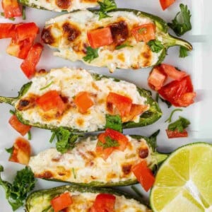 Close up of grilled jalapeño poppers with golden melted cheese, diced tomatoes, and fresh herbs