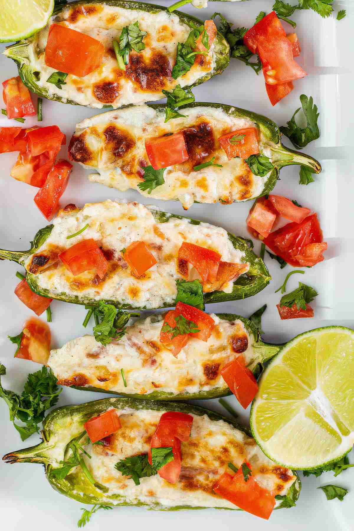 Close up of grilled jalapeño poppers with golden melted cheese, diced tomatoes, and fresh herbs