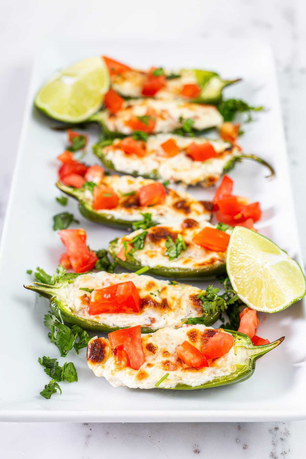 Grilled jalapeño poppers with melted cheese, tomatoes, cilantro, and lime ready to serve