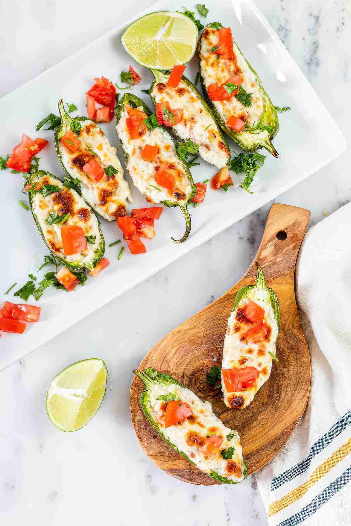 Grilled jalapeño poppers filled with creamy cheese and bacon, topped with fresh tomato, cilantro, and lime on a serving platter
