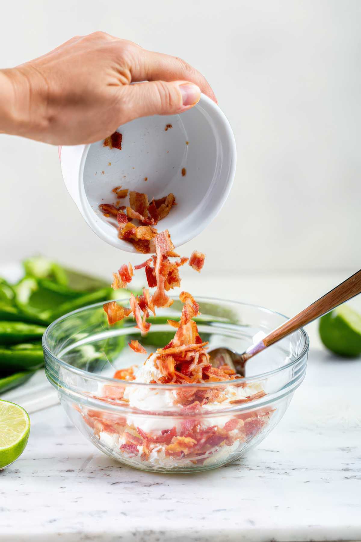 Adding chopped bacon to cream cheese mixture for grilled jalapeño poppers filling