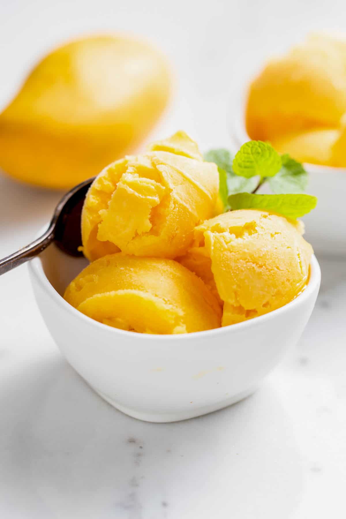 A bowl filled with three scoops of homemade mango sorbet sitting on a white tabletop.