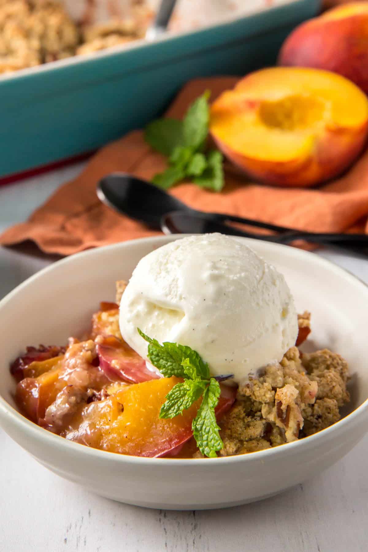 a bowl of peach cobbler on a countertop with a scoop of vanilla ice cream