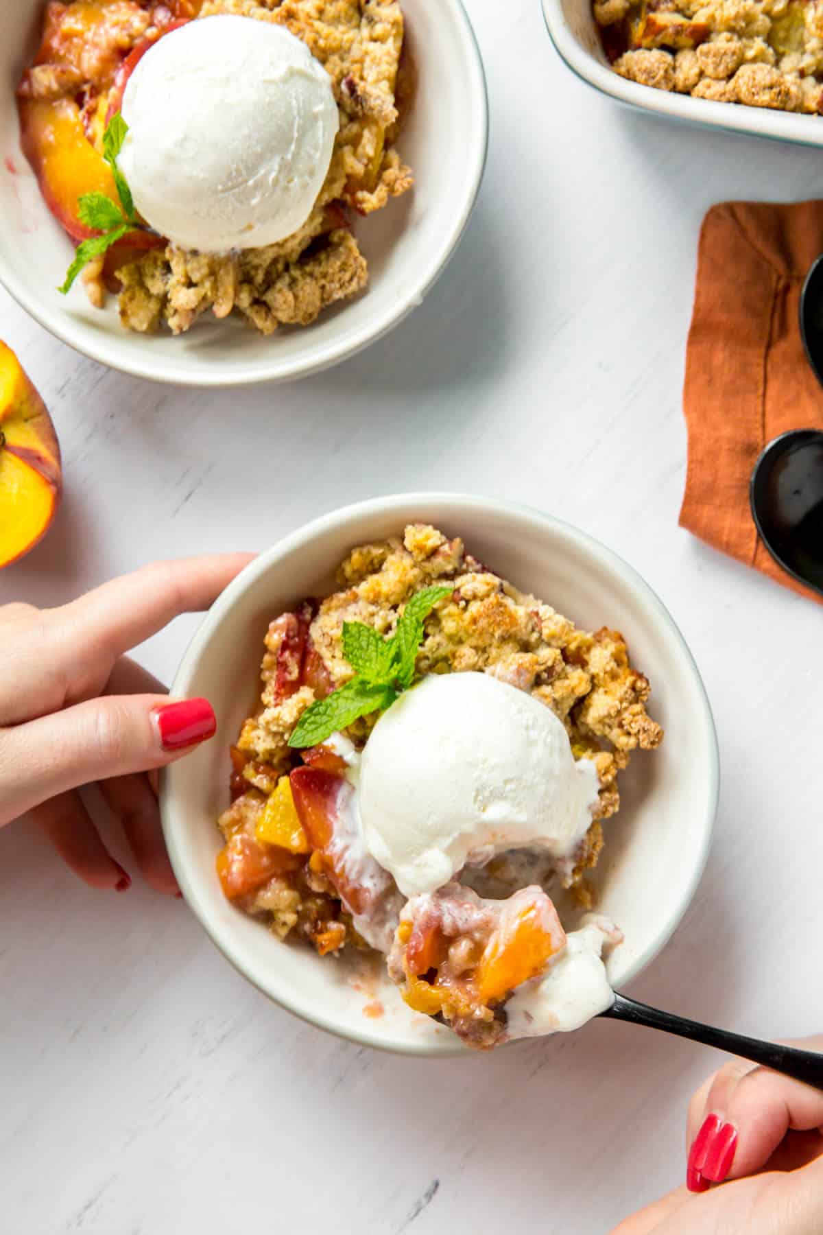 two bowls of peach crumble in a bowl with a scoop of vanilla ice cream on top