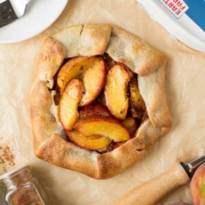 Rustic peach crostata on parchment paper with fresh peaches and baking ingredients