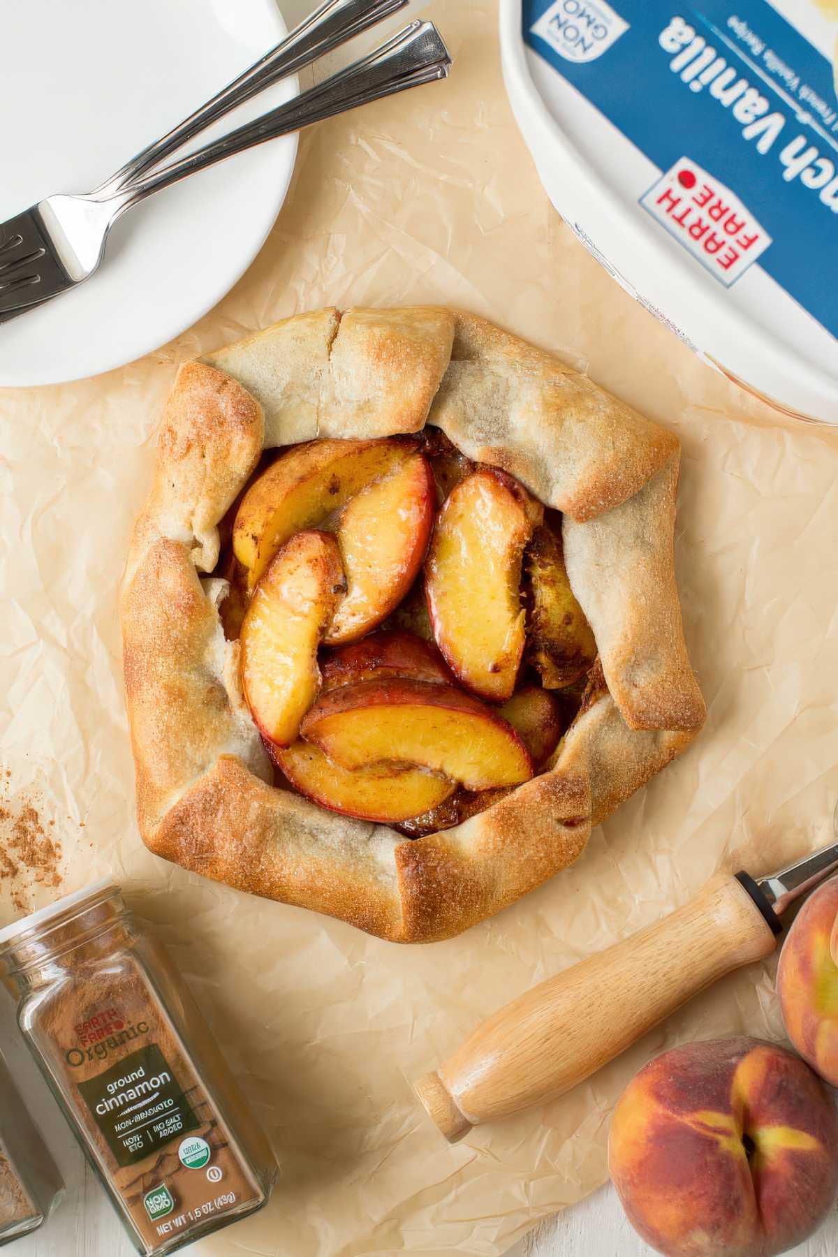 Rustic peach crostata on parchment paper with fresh peaches and baking ingredients