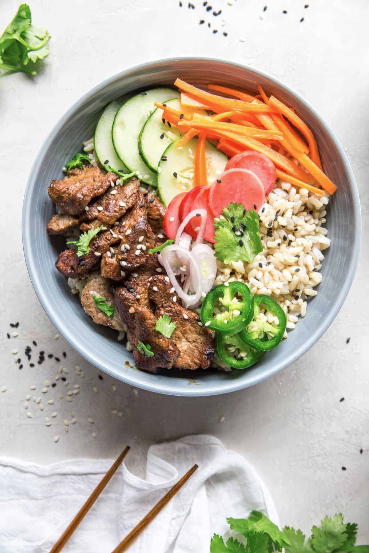 Healthy Banh Mi bowl with brown rice, pork tenderloin, carrots, radishes, cucumber, and jalapeños