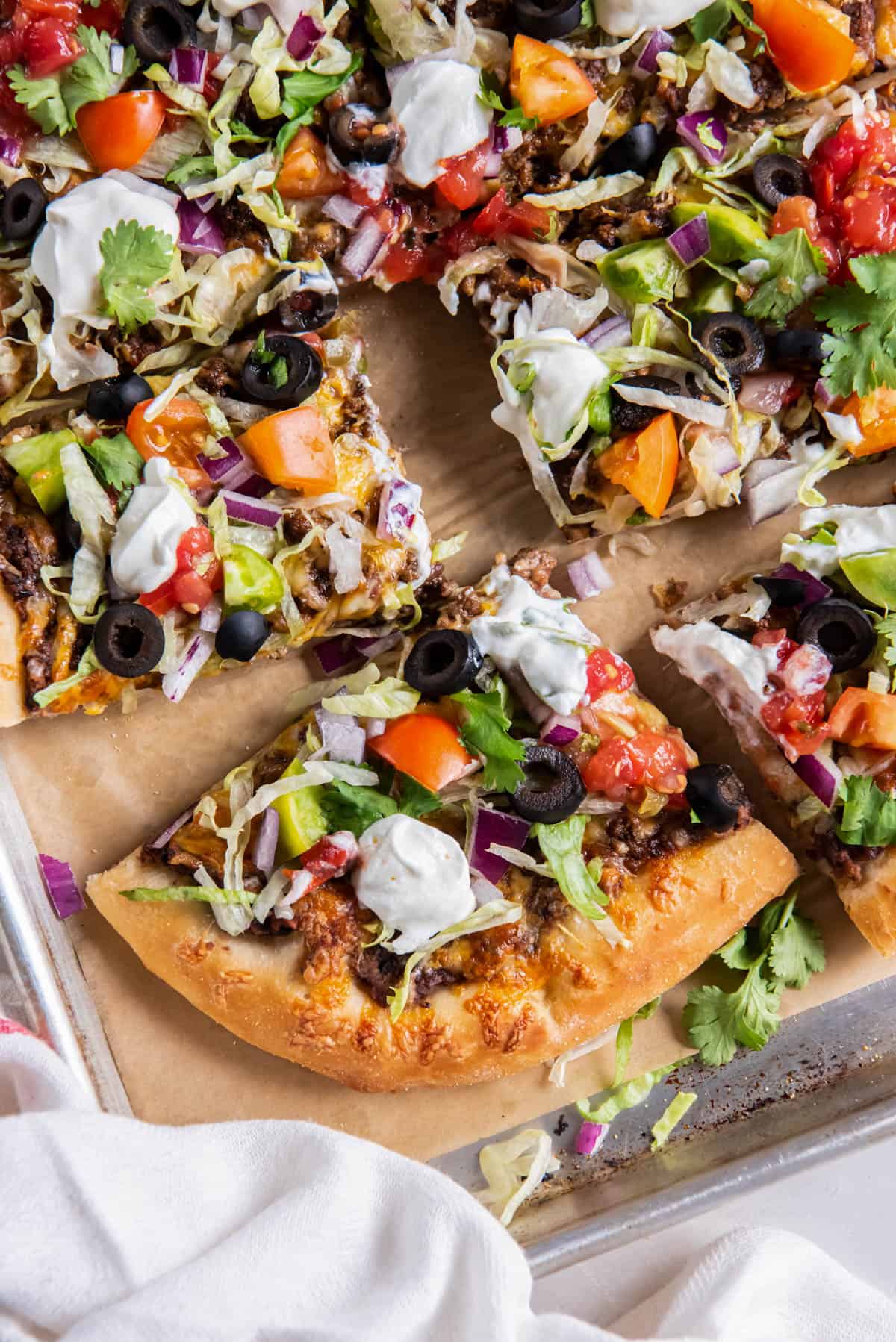 Taco pizza is cut into slices on a piece of parchment paper before serving.