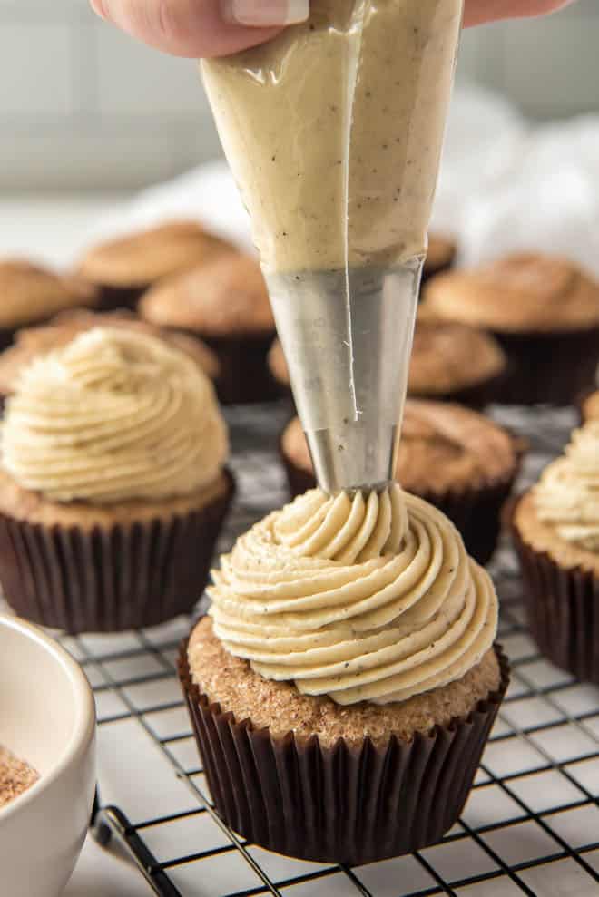 Piping brown buttercream frosting onto snickerdoodle cupcakes