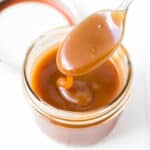 a jar of homemade caramel sauce with a spoon of sauce