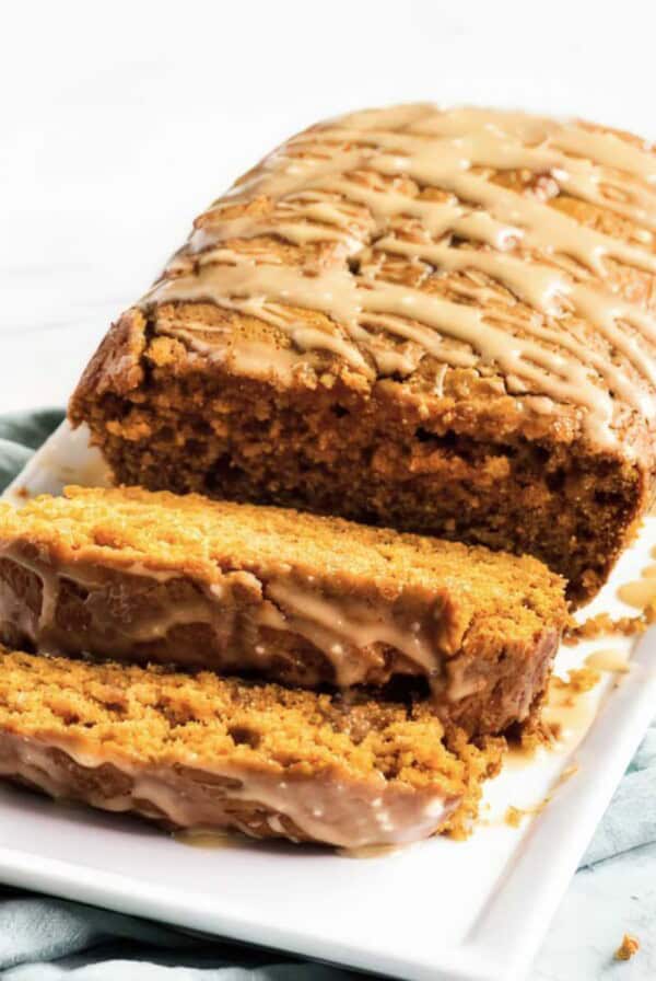 Sliced moist pumpkin bread with maple glaze drizzled on top, showing soft texture inside the loaf.