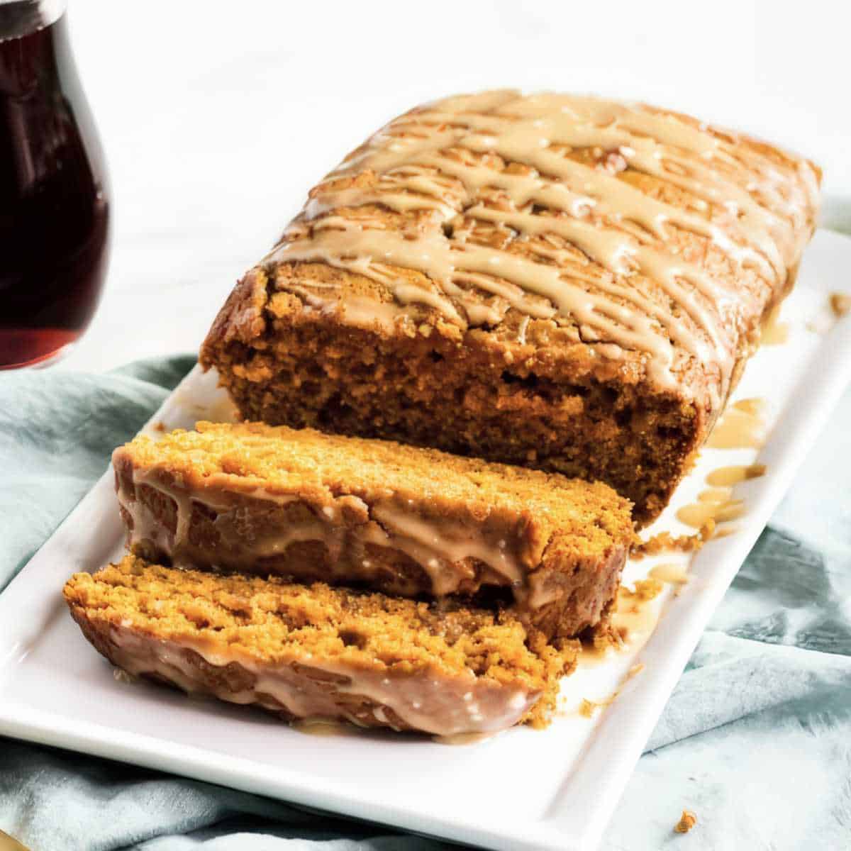 Sliced moist pumpkin bread with maple glaze drizzled on top, showing soft texture inside the loaf.