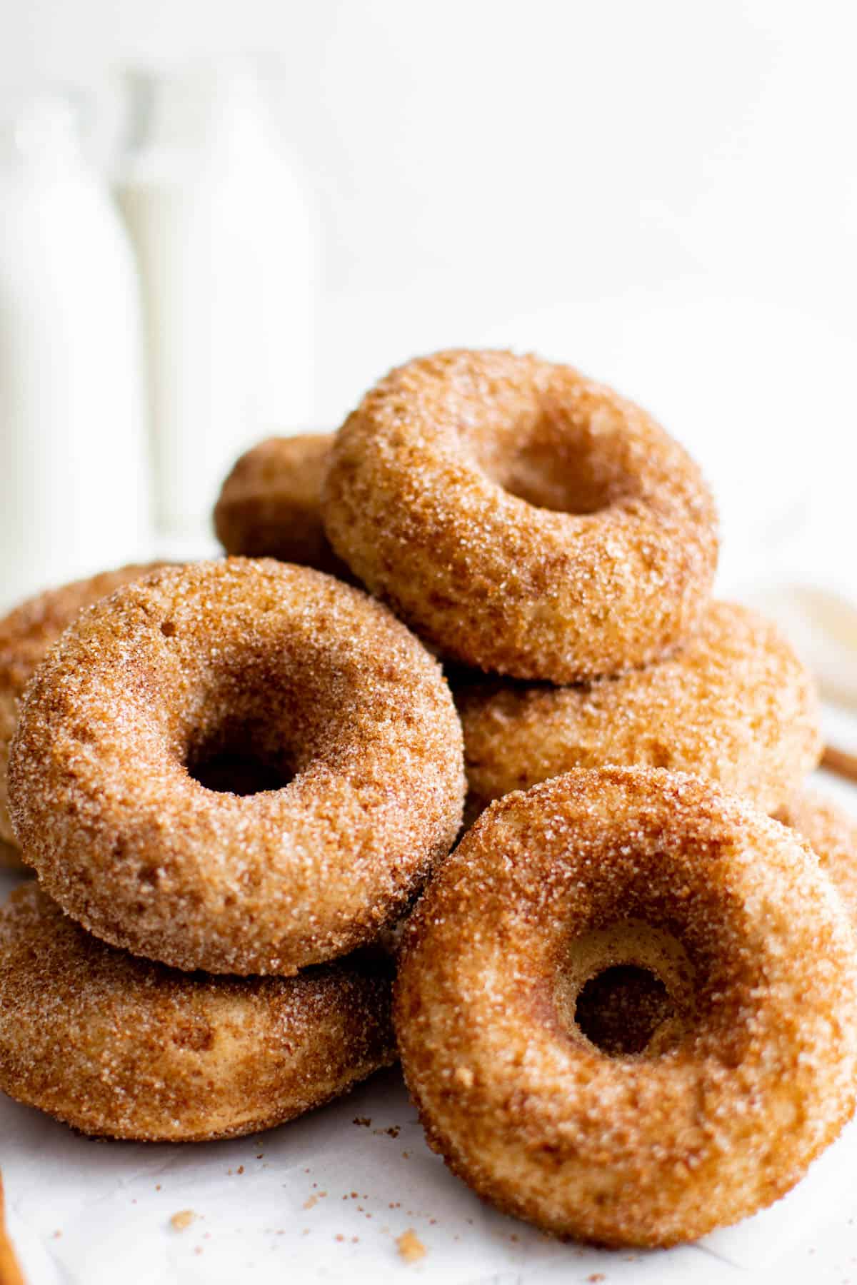 a pile of apple cider donuts next to a glass milk jug