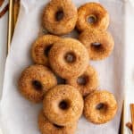 a pile of apple cider donuts on a piece of parchment paper on a baking sheet