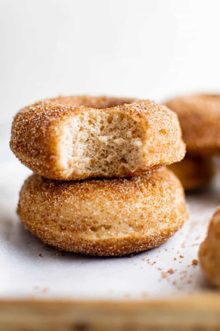 Stack of baked apple cider donuts coated in cinnamon sugar served on parchment paper.