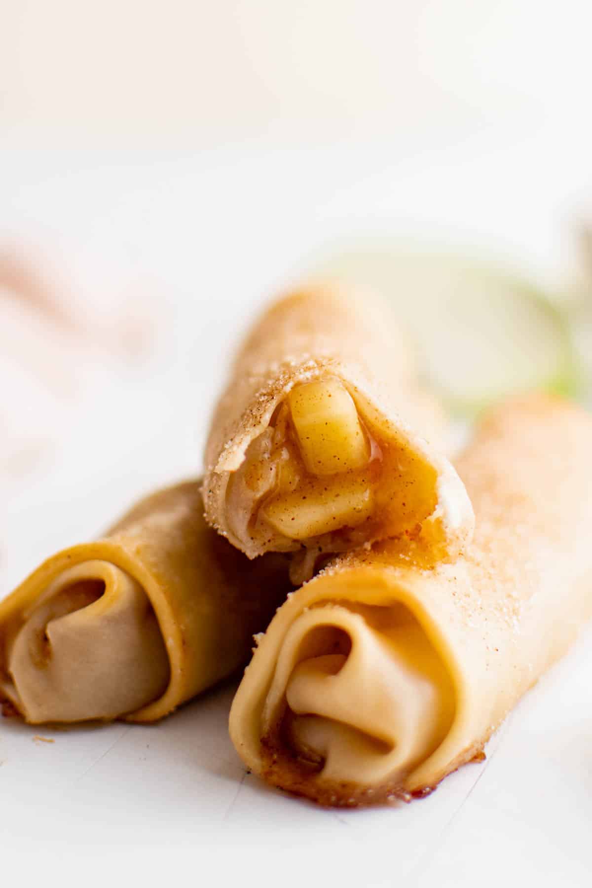 Three baked apple pie egg rolls sitting on a white countertop.