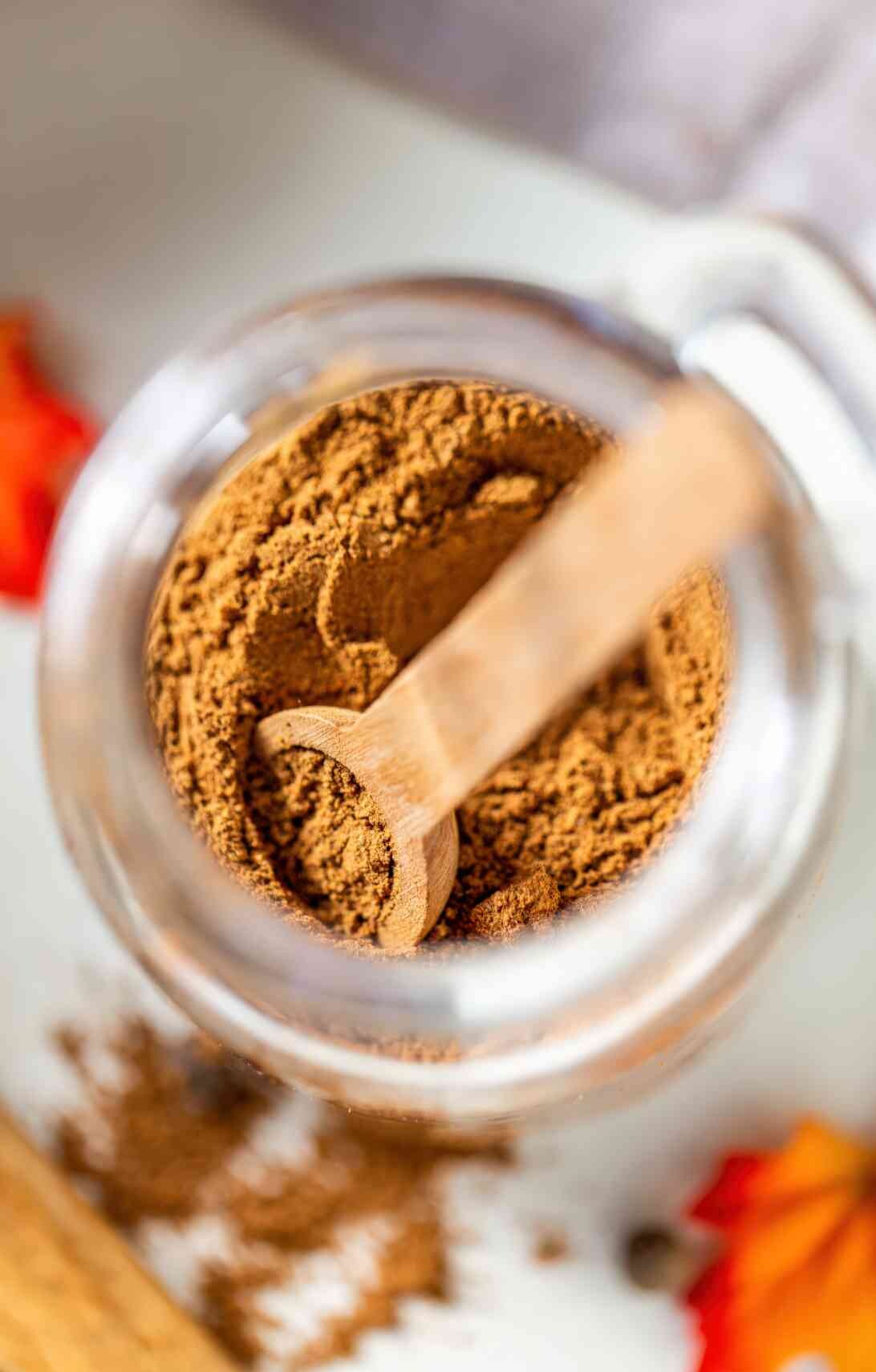 Overhead view of a wooden scoop resting in a jar of freshly mixed homemade pumpkin pie spice blend