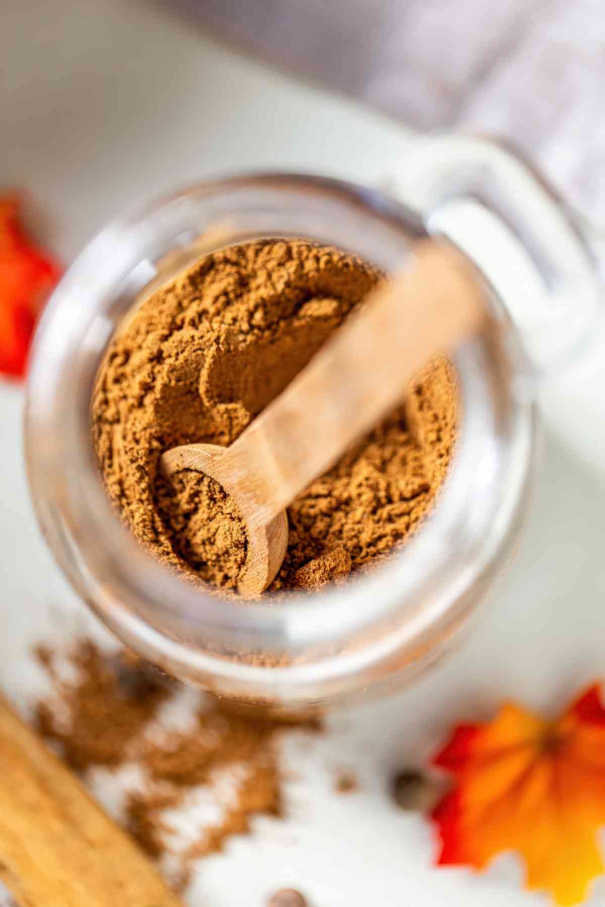 Overhead view of a wooden scoop resting in a jar of freshly mixed homemade pumpkin pie spice blend