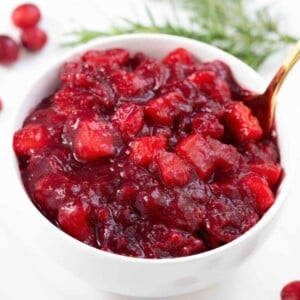 orange apple cranberry sauce in a white bowl with a spoon.