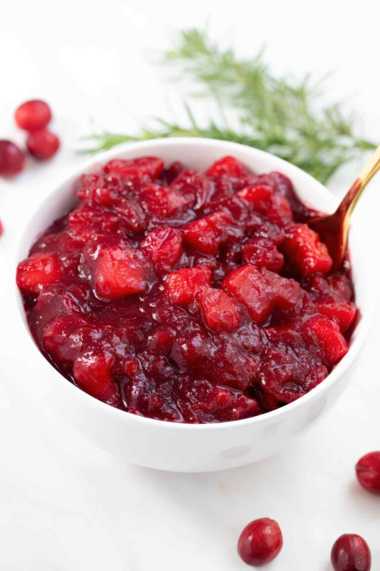 orange apple cranberry sauce in a white bowl with a spoon.